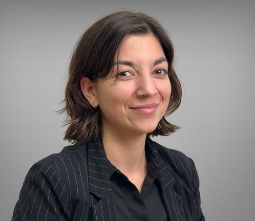 Portrait von Julia Kreuzer. Sie hat schulterlange braune Haare und ein Nasenpiercing. Sie trägt ein schwarzes Hemd mit einem schwarzen Blazer.