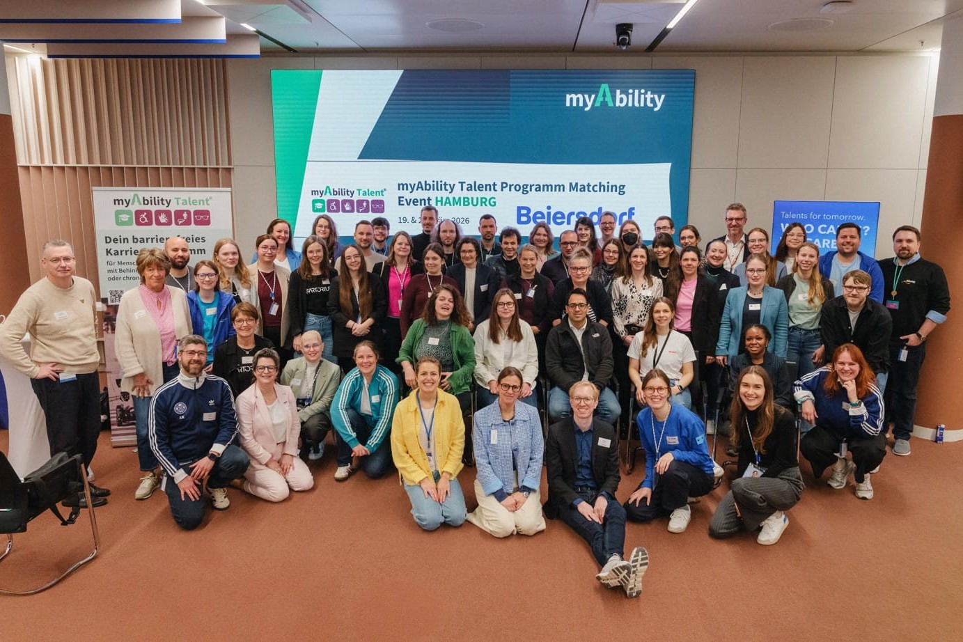 Gruppenfoto des Matching Days. Im Hintergrund auf einem Bildschirm eine Präsentation mit dem Logo von myAbility und Beiersdorf.