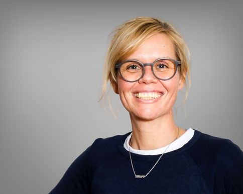Eine als Frau gelesene Person mit blonden Haaren lächelt.